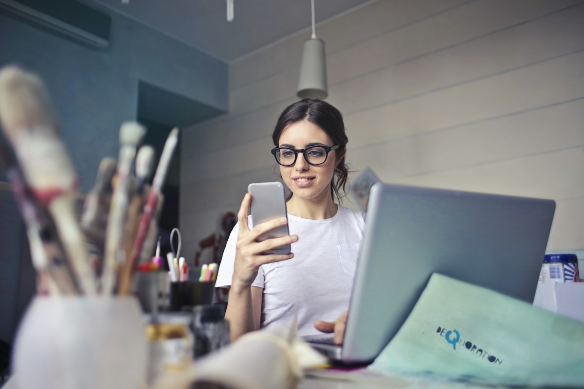 Emprendedora revisando su web en el móvil junto a su portátil